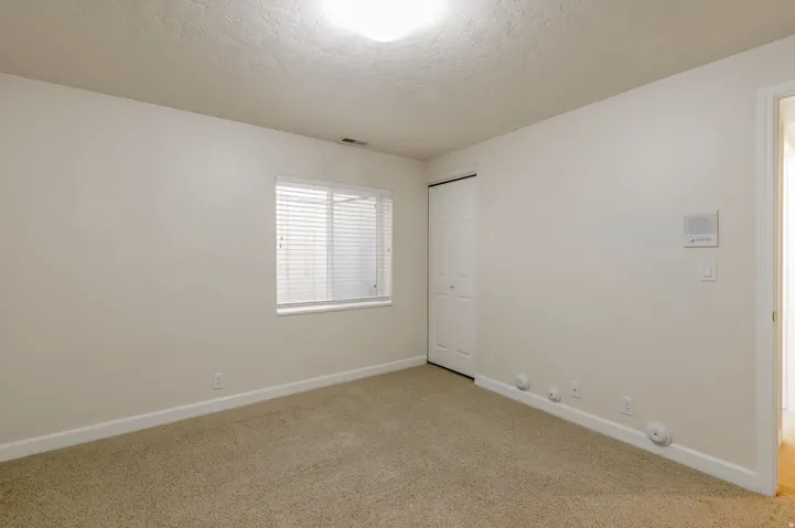 Neutral-toned room featuring a single window with blinds, carpet flooring, and a bi-fold closet door