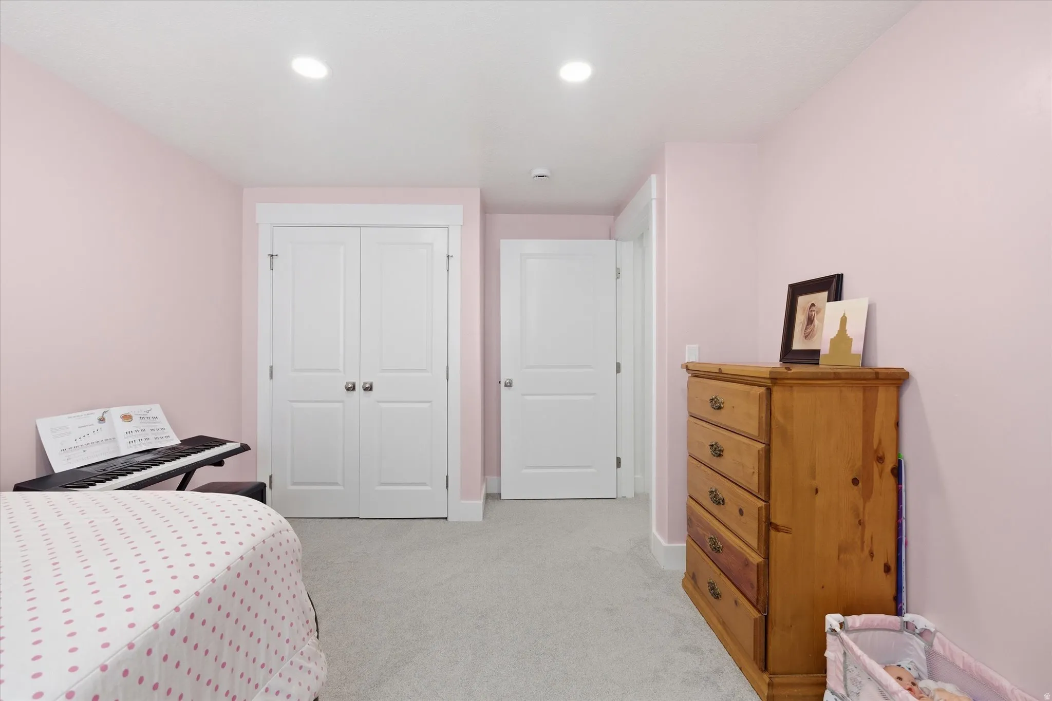 Recessed lighting illuminates a room featuring light pink walls and light gray carpet flooring