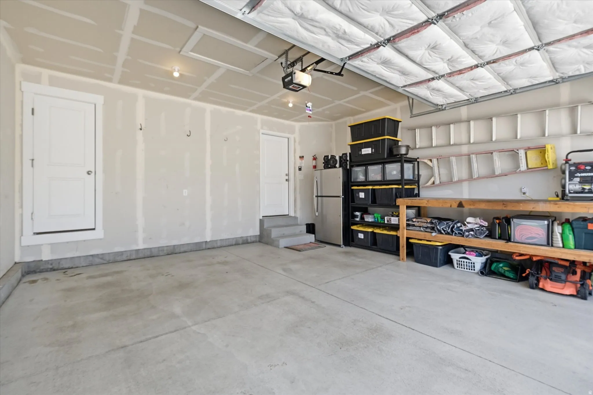 Concrete flooring garage featuring a drywall-finished ceiling, two interior access doors, and an overhead garage door with insulation panels