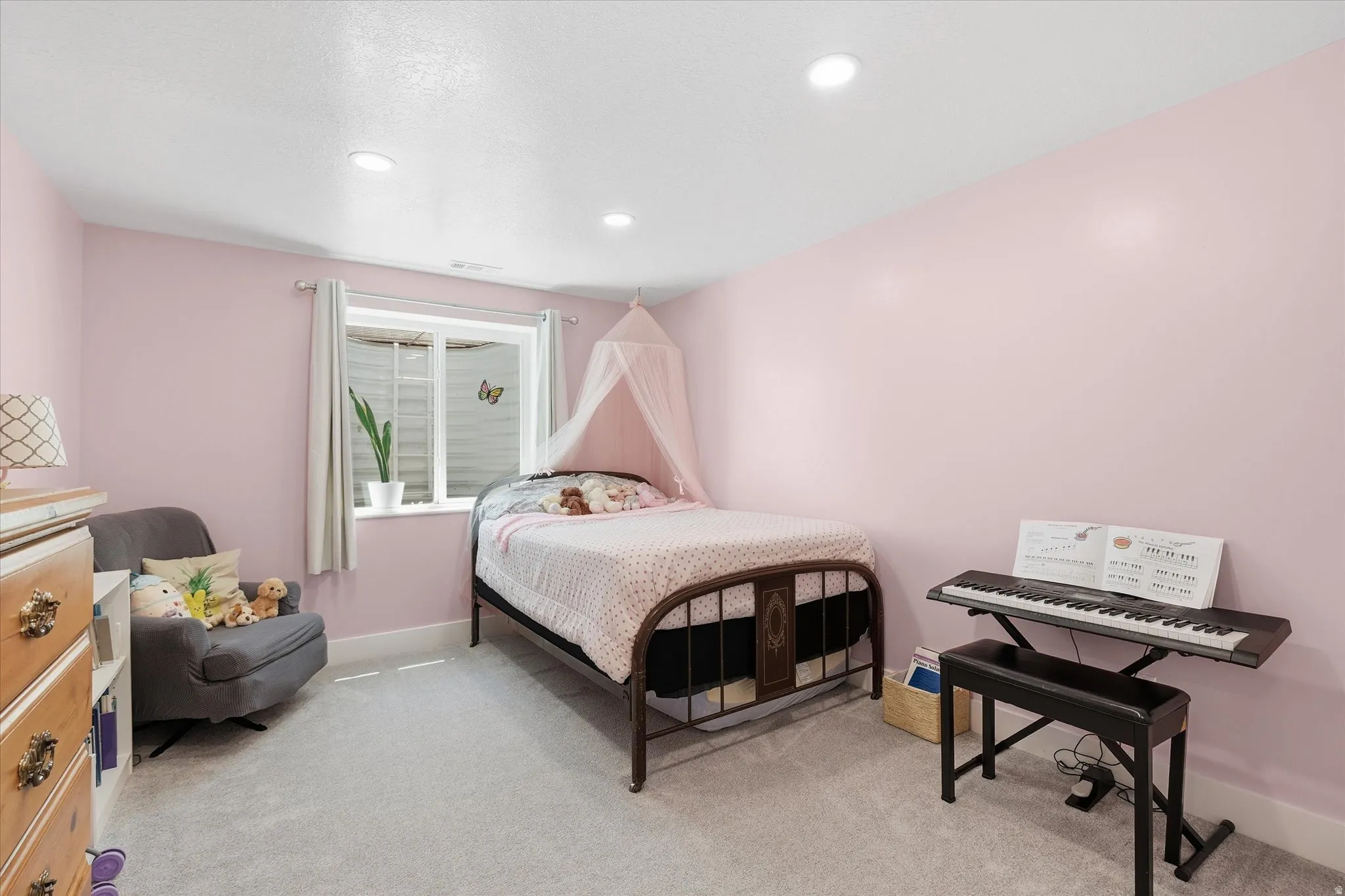 Recessed lighting illuminates this room, featuring light pink walls, light gray carpeting, and a white-trimmed window