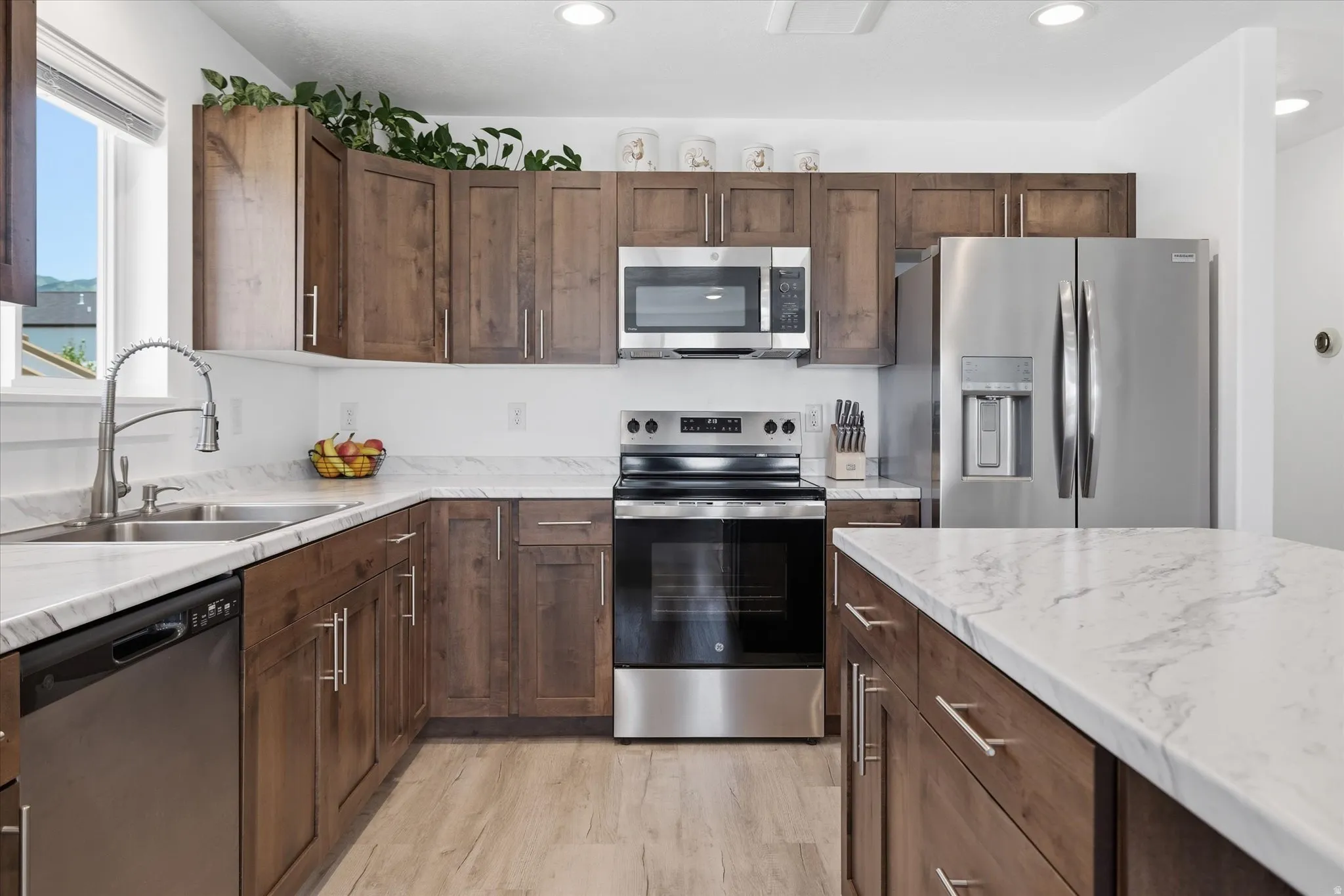 Kitchen featuring wood-finish cabinetry, white countertops, stainless steel appliances, and light wood-finish flooring