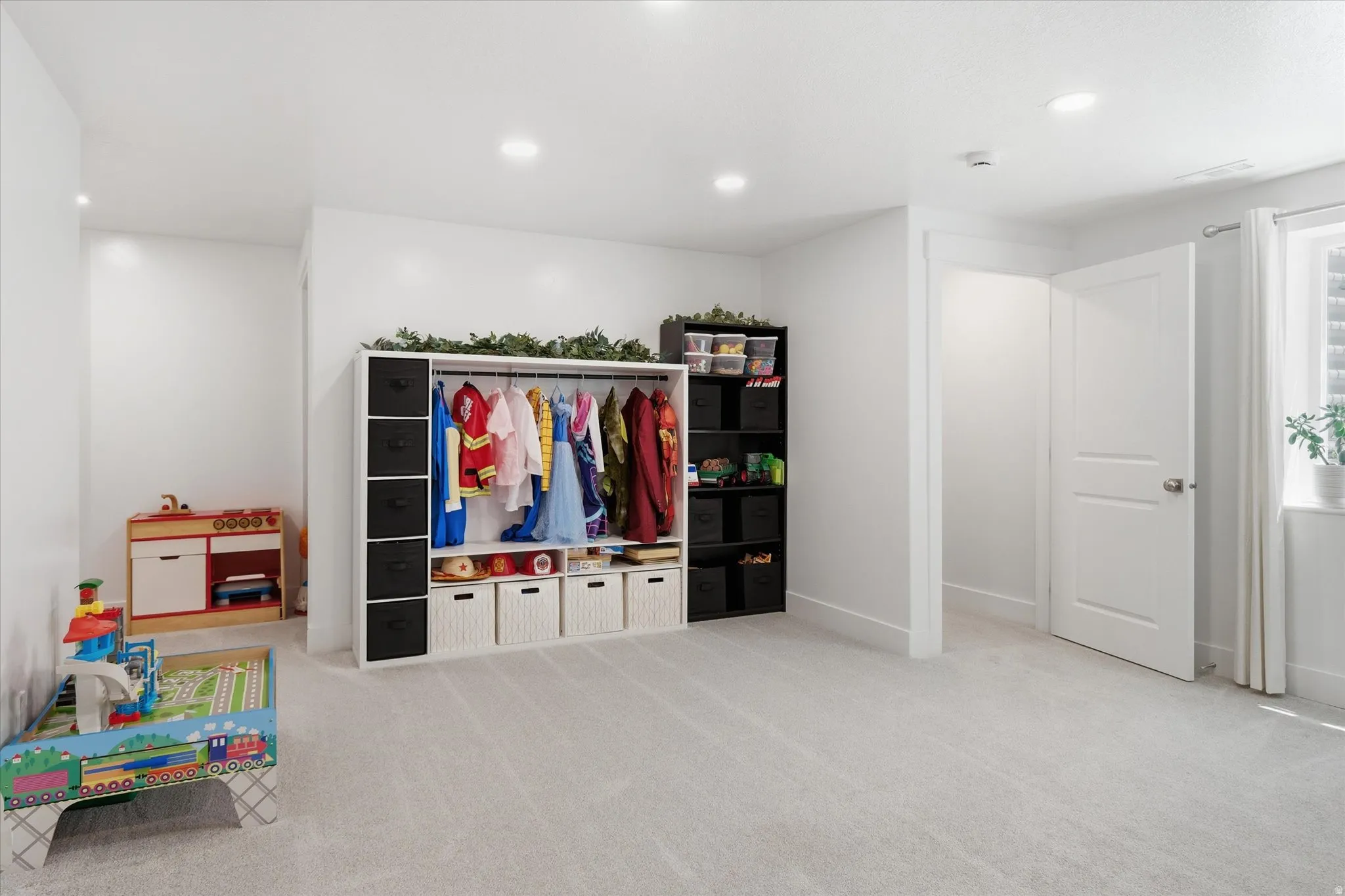 Expansive carpeted room featuring recessed lighting, a white painted door, and a window with white blinds