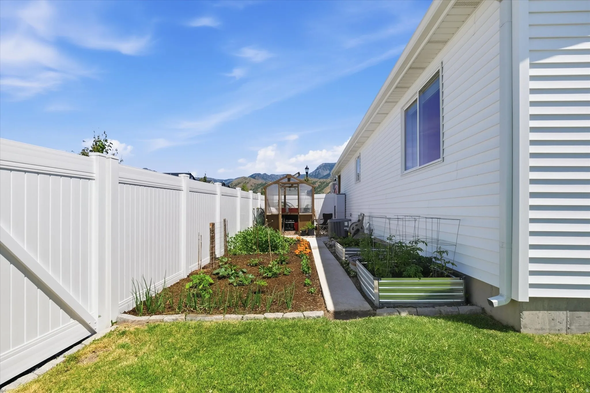 Manicured yard area featuring a robust white vinyl privacy fence, a dedicated garden bed, and a greenhouse structure