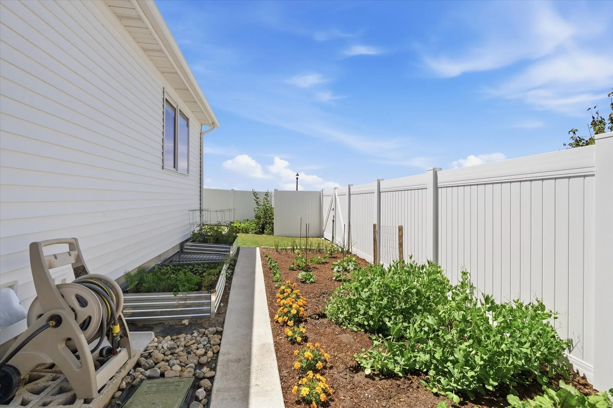 Established garden beds featuring a variety of plantings, bordered by a white vinyl privacy fence