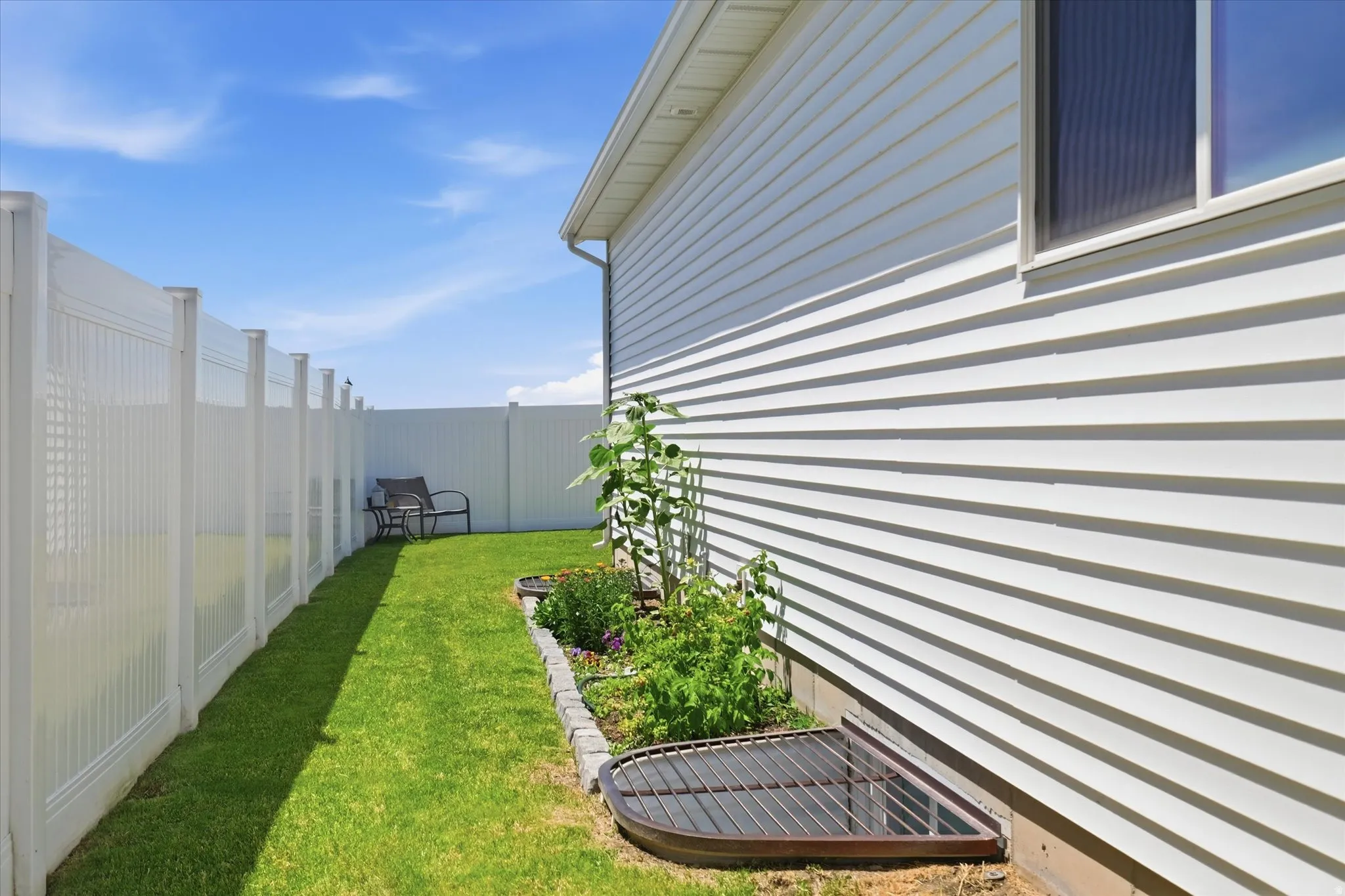 Side yard featuring a vinyl privacy fence, manicured lawn, and a garden bed bordering the home's white siding