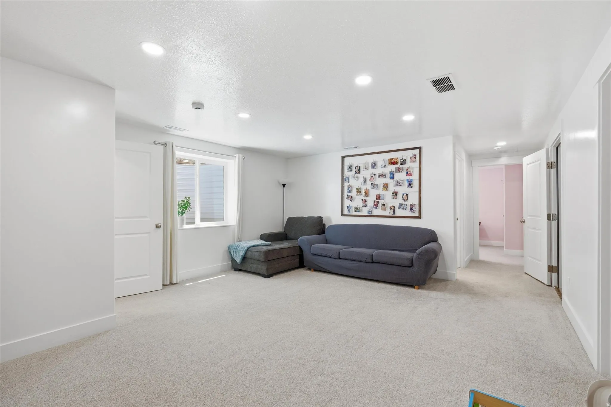 Spacious carpeted room featuring white walls, recessed lighting, and a window with horizontal blinds
