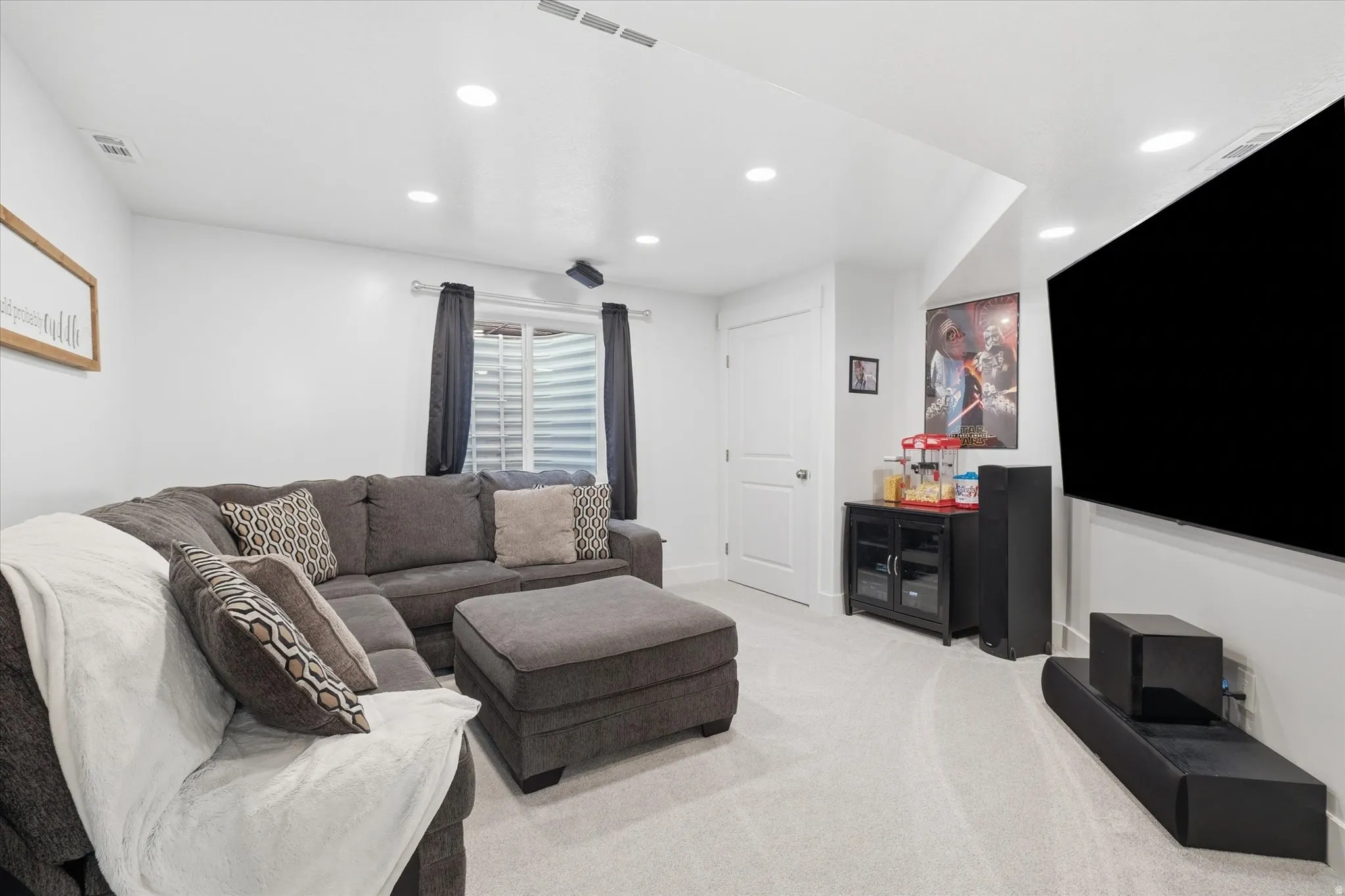 Carpeted lower-level living area with recessed lighting, white walls, and a window featuring horizontal blinds