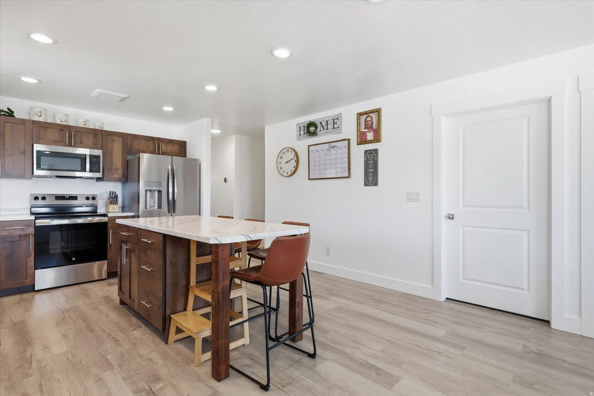 Kitchen featuring a central island with a stone look countertop, recessed lighting, wood-finish flooring, stainless steel appliances, and dark wood cabinetry