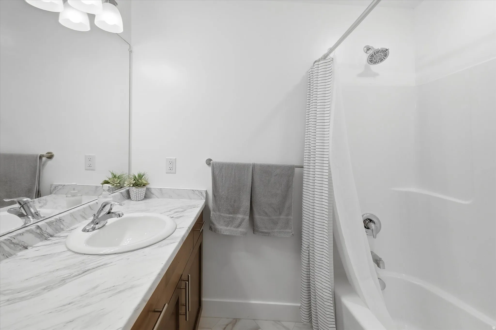 Bathroom featuring a white bathtub with shower, chrome fixtures, and a white vanity with an undermount sink and marble-look countertop