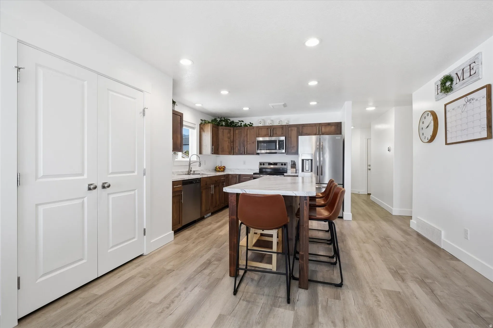 Spacious kitchen featuring wood-finish cabinetry, stainless steel appliances, a center island with a light-toned countertop, and light wood-finish flooring