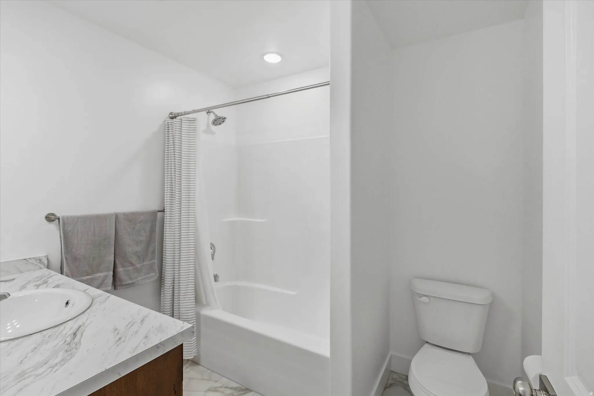 Bathroom featuring a white bathtub and shower combination with a curved shower curtain rod, a single vanity with a white rectangular sink, a white marble-finish countertop, and a wood-finish vanity cabinet