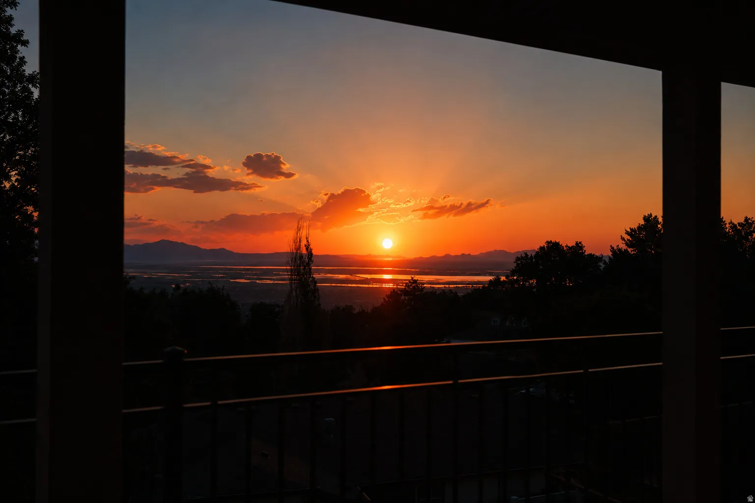 Expansive outdoor space featuring a balcony with metal railings and a panoramic sunset over a body of water with distant mountains