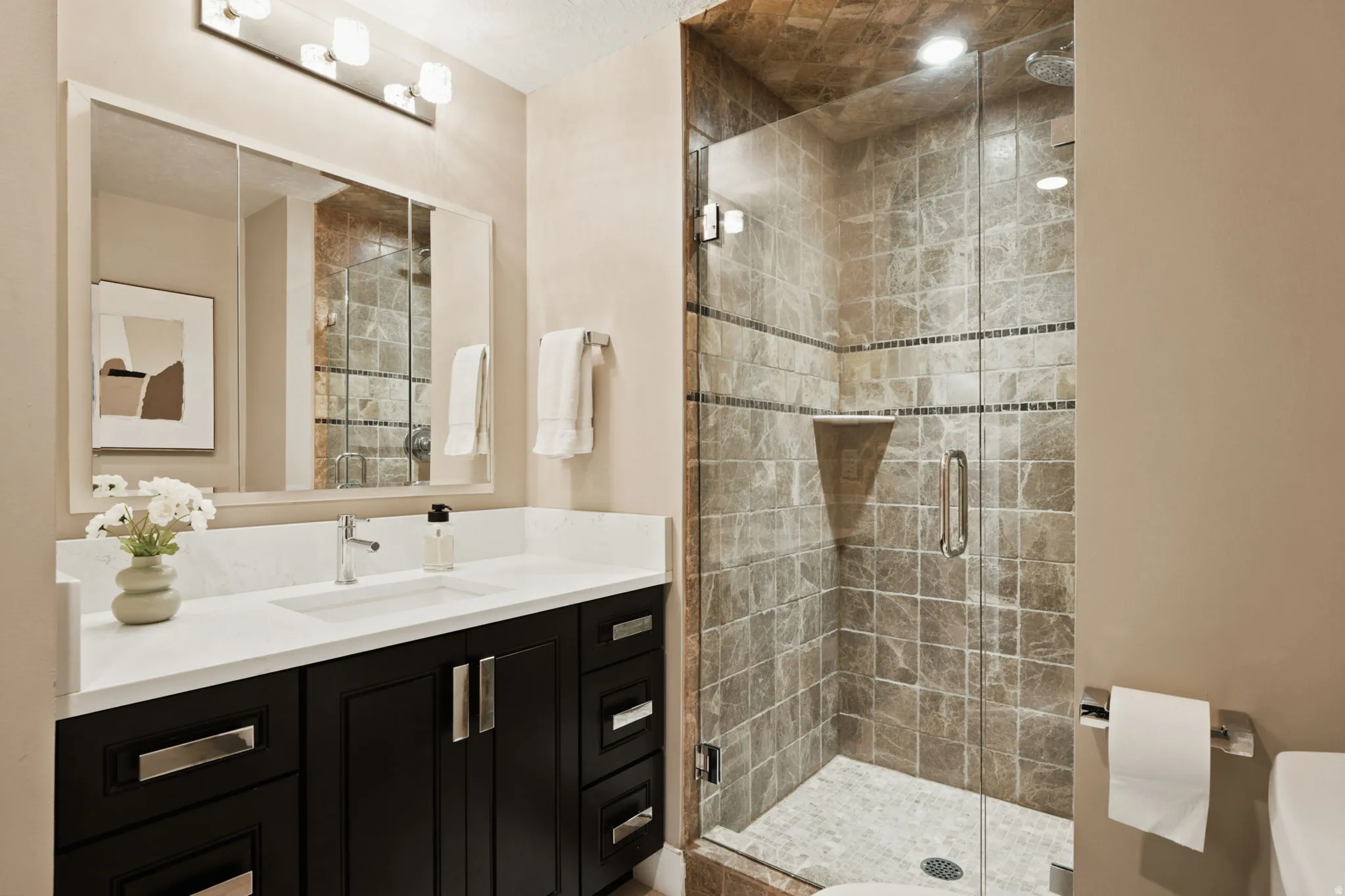 Contemporary bathroom featuring a dark wood-finish vanity with a white countertop and undermount sink, a large framed mirror, and an illuminated shower with tile surround and glass enclosure