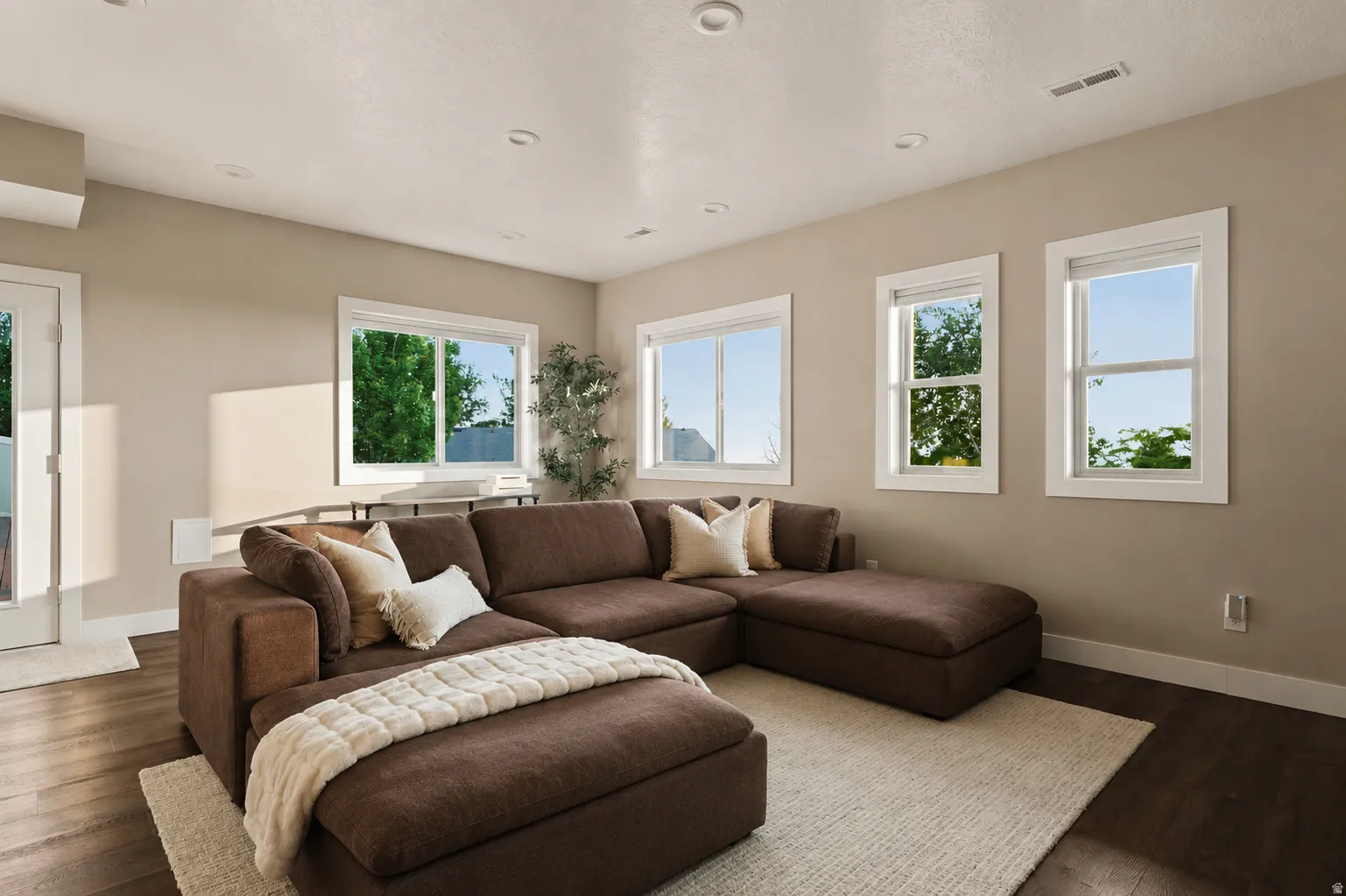 Spacious living area featuring wood-finish flooring, recessed lighting, and multiple windows with white trim