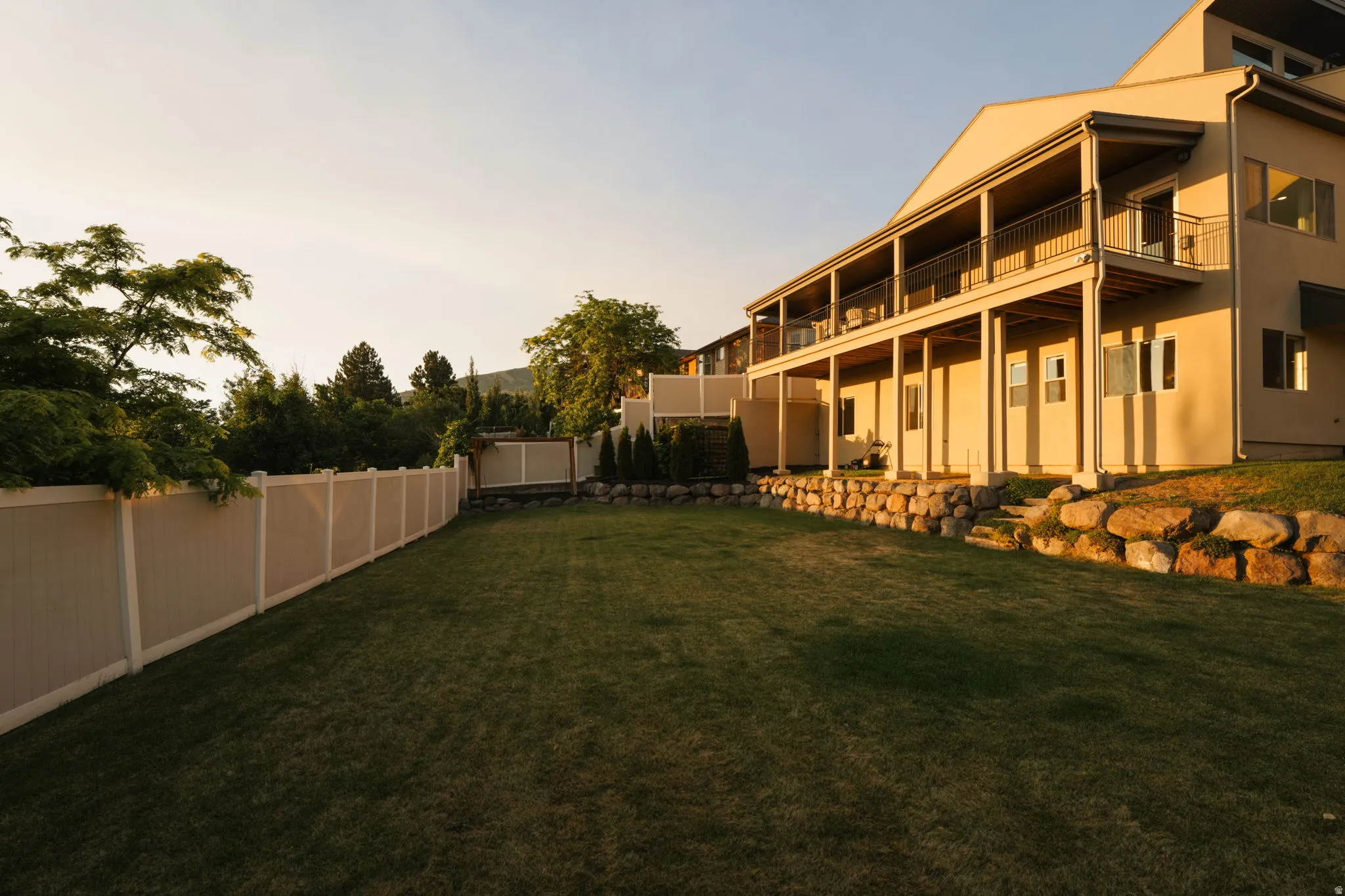 Spacious backyard featuring a manicured lawn, a full privacy fence, and a multi-level rock retaining wall