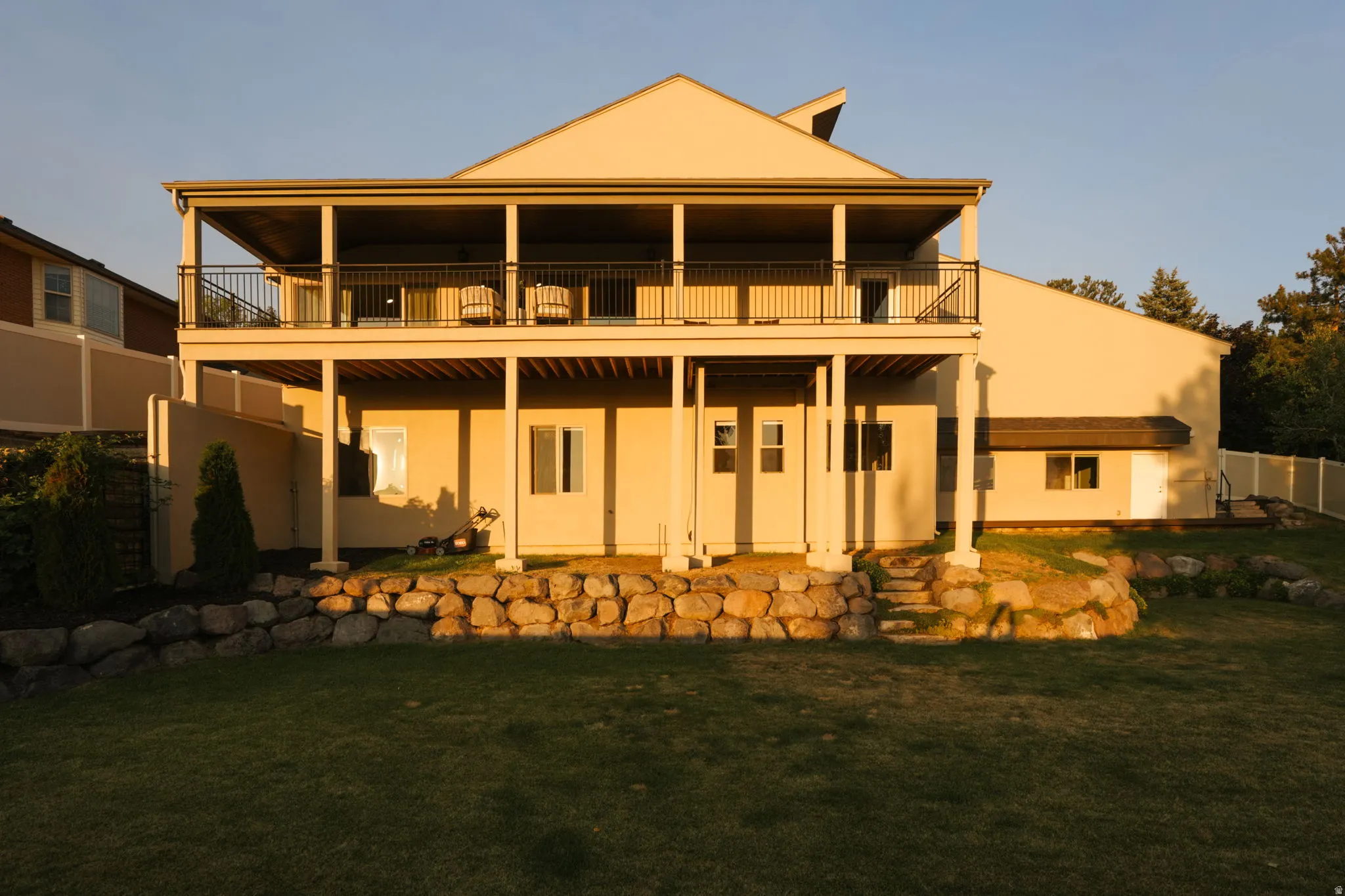 Multi-level exterior featuring a covered upper-level balcony with black metal railings, supported by substantial columns