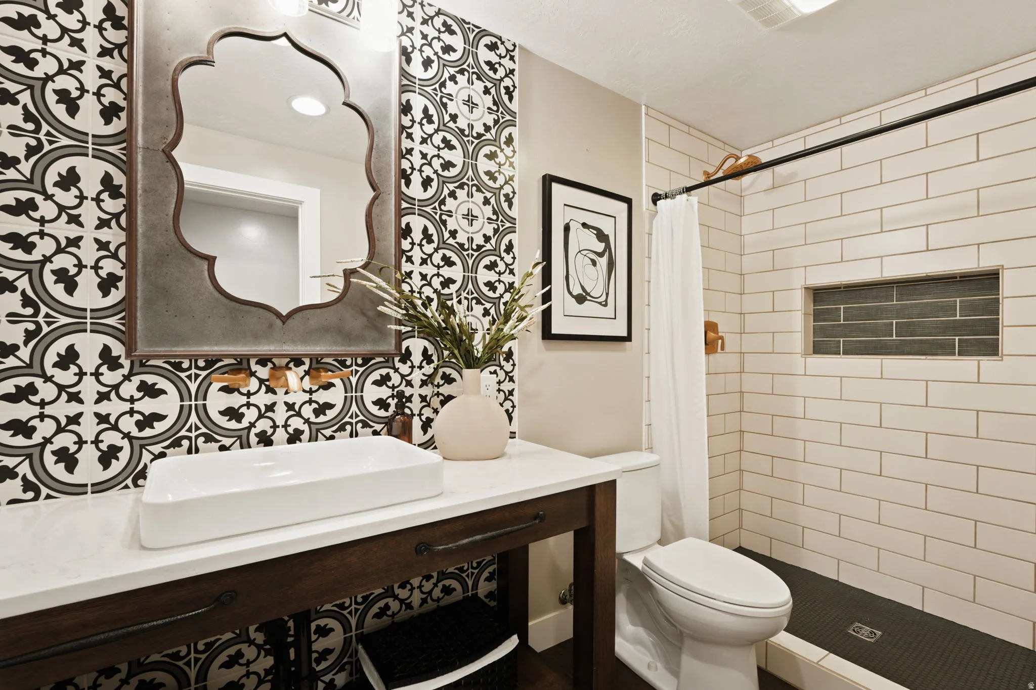 Bathroom featuring a vanity with a white countertop and rectangular vessel sink, a decorative wall mirror, and a tiled shower with a built-in niche