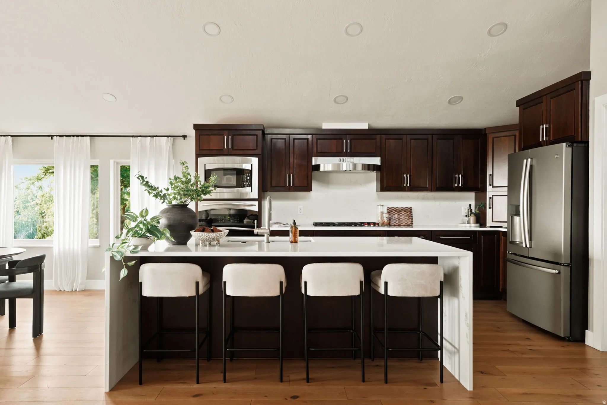 Kitchen featuring a central island with white countertop, dark wood cabinetry, stainless steel appliances, recessed lighting, and wood-finish flooring