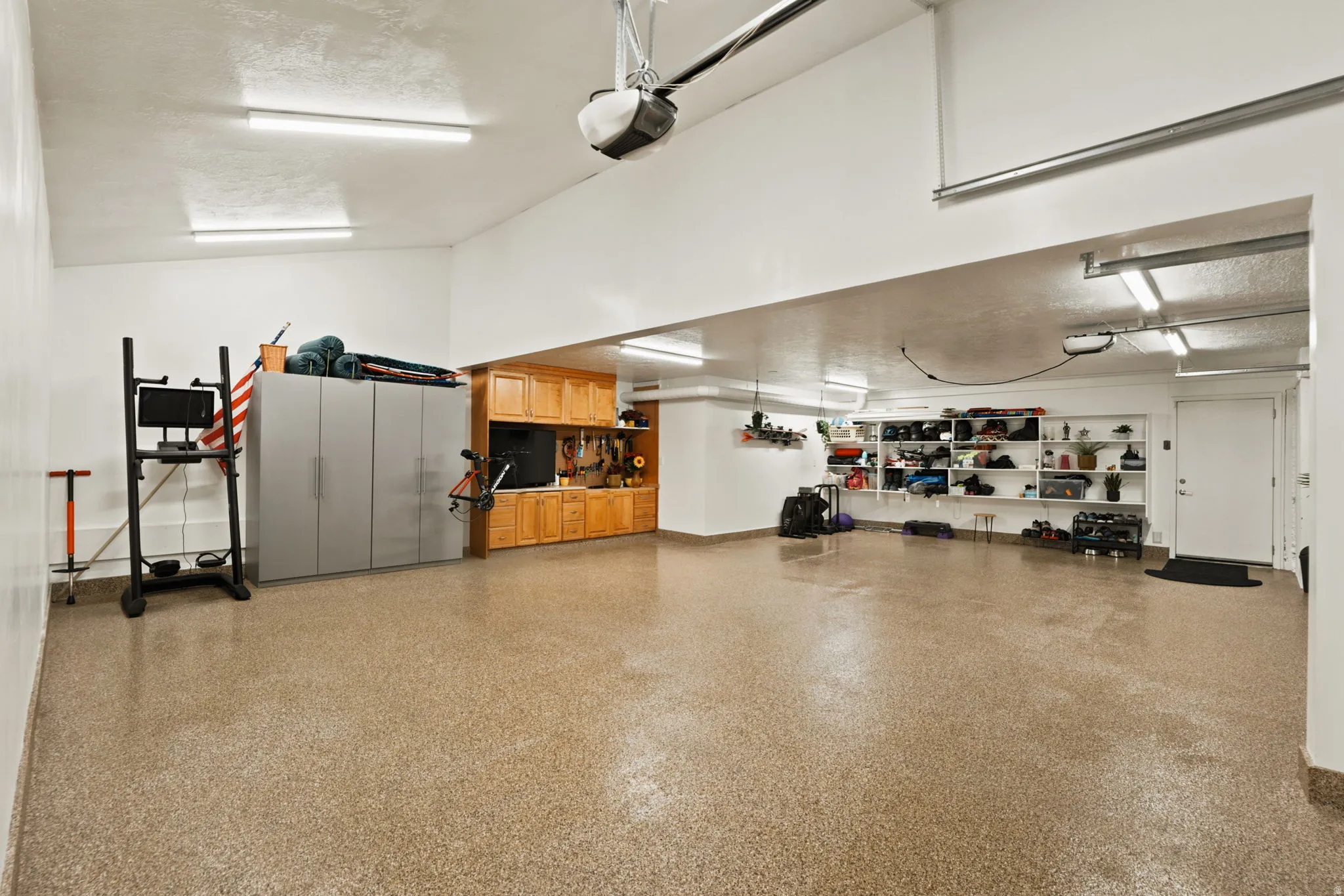 Spacious garage featuring a speckled epoxy floor, built-in wooden cabinetry, wall-mounted shelving, and bright overhead strip lighting