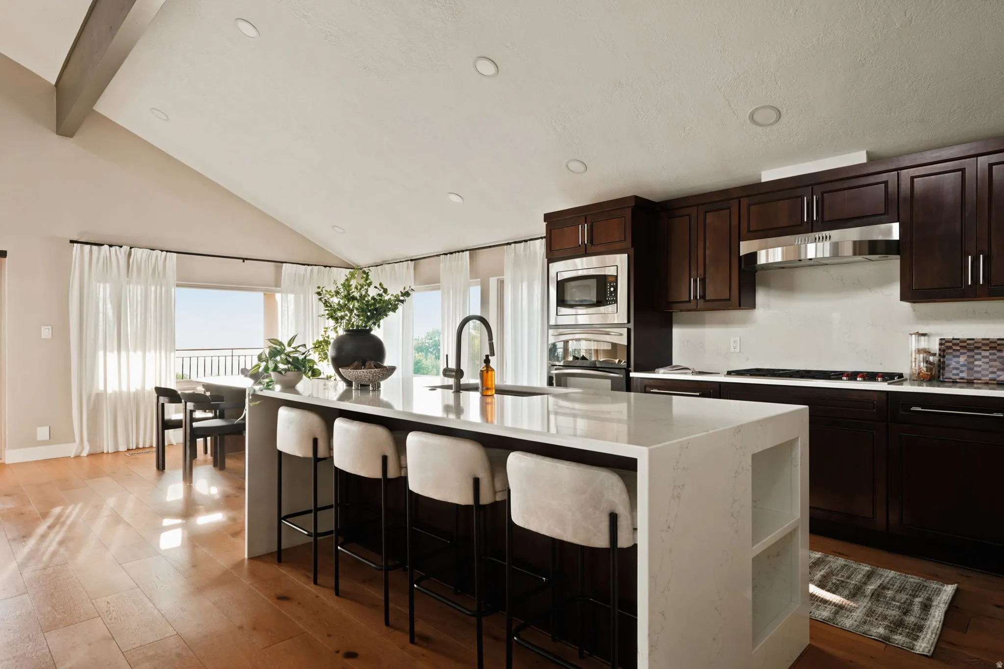 Open-concept kitchen featuring an expansive island with seating, dark wood cabinetry, and integrated stainless steel appliances