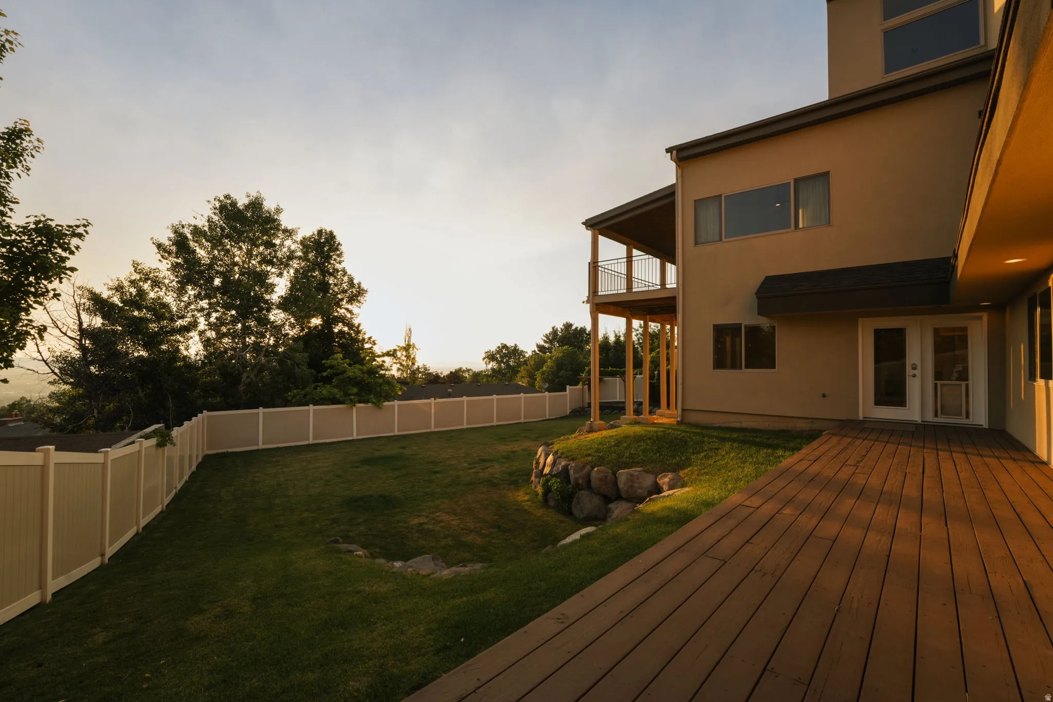 Spacious rear yard with a wood-finish deck, privacy fencing, and a terraced rock garden