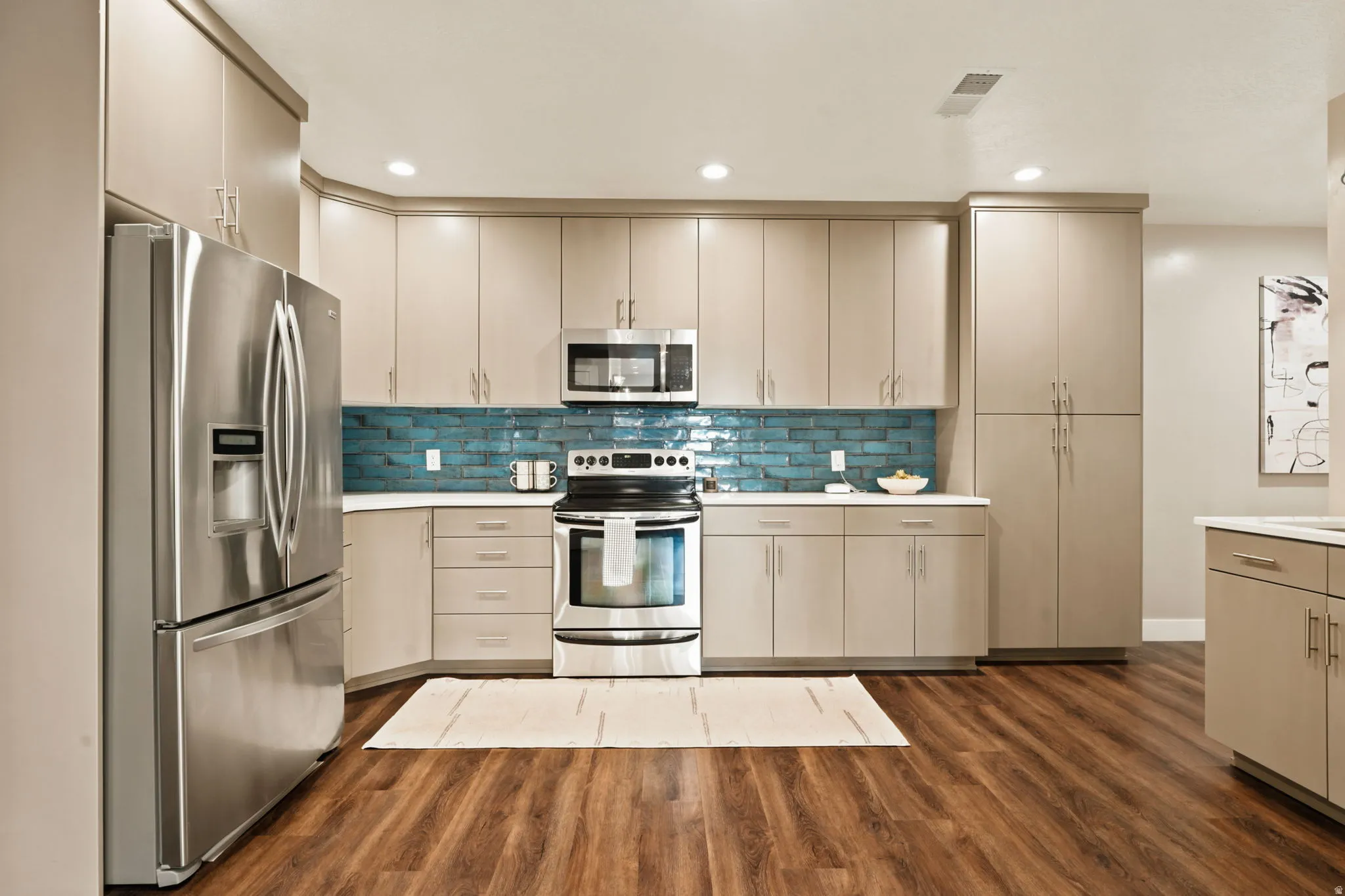 Modern kitchen featuring wood-finish flooring, stainless steel appliances, a vibrant blue tile backsplash, light-toned cabinetry, and recessed lighting