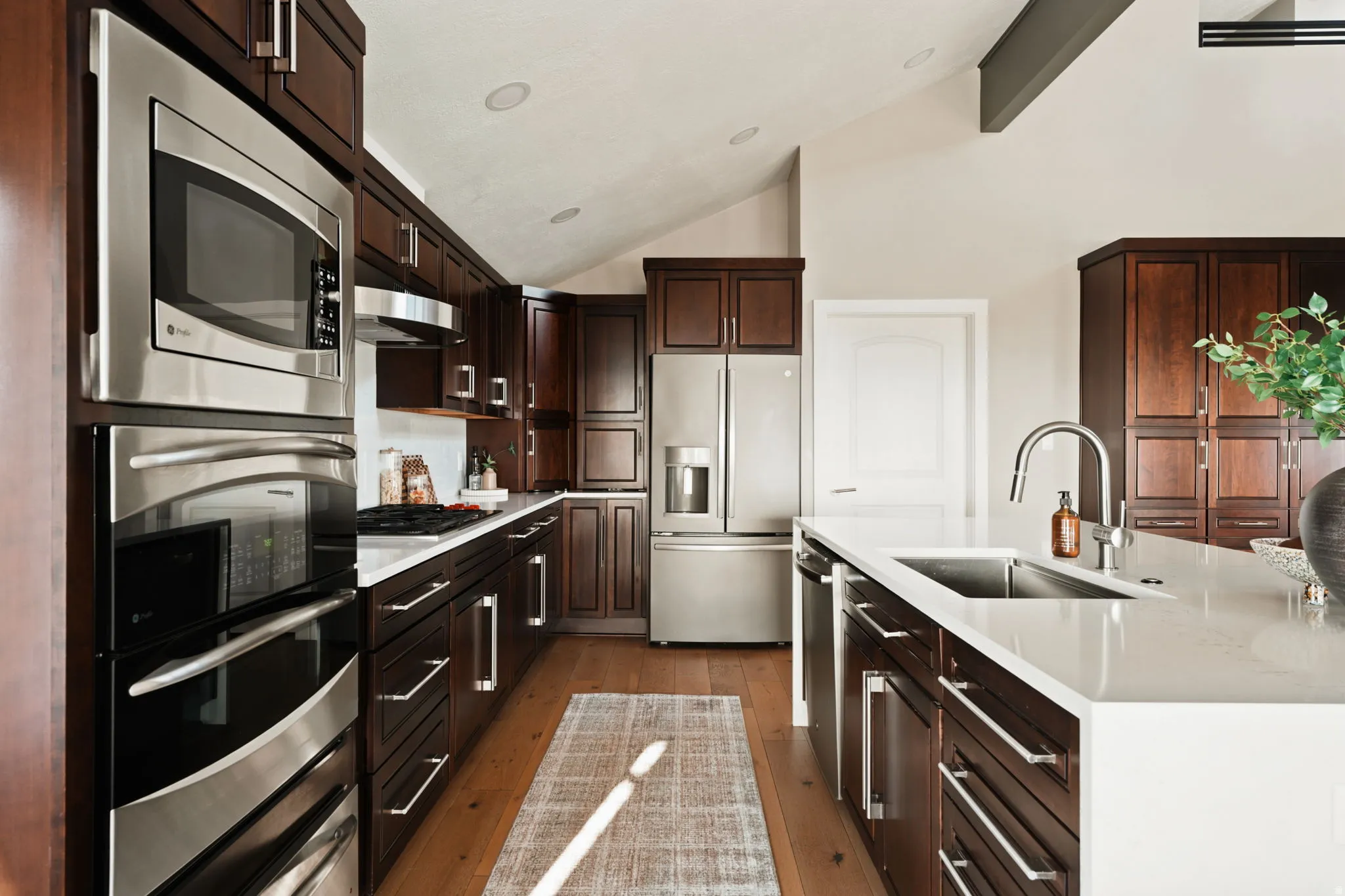 Kitchen featuring dark wood cabinetry, stainless steel appliances, light-toned countertops, and wood-finish flooring