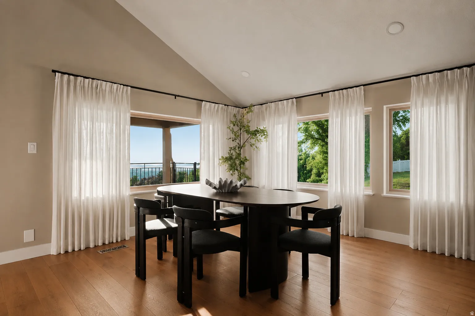Vaulted ceiling dining area featuring light-toned walls, wood-finish flooring, recessed lighting, and multiple windows with sheer white drapery