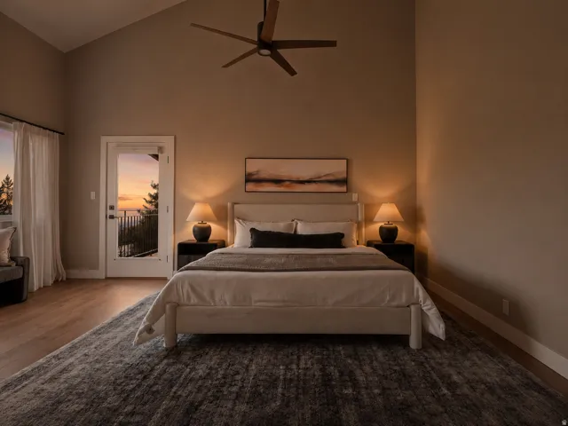 Vaulted ceiling bedroom featuring wood-finish flooring, a ceiling fan, and a glass-paneled door leading to an outdoor balcony with metal railings