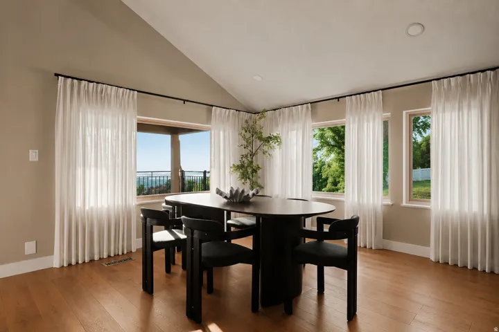 Vaulted ceiling dining area featuring light-toned walls, wood-finish flooring, recessed lighting, and multiple windows with sheer white drapery