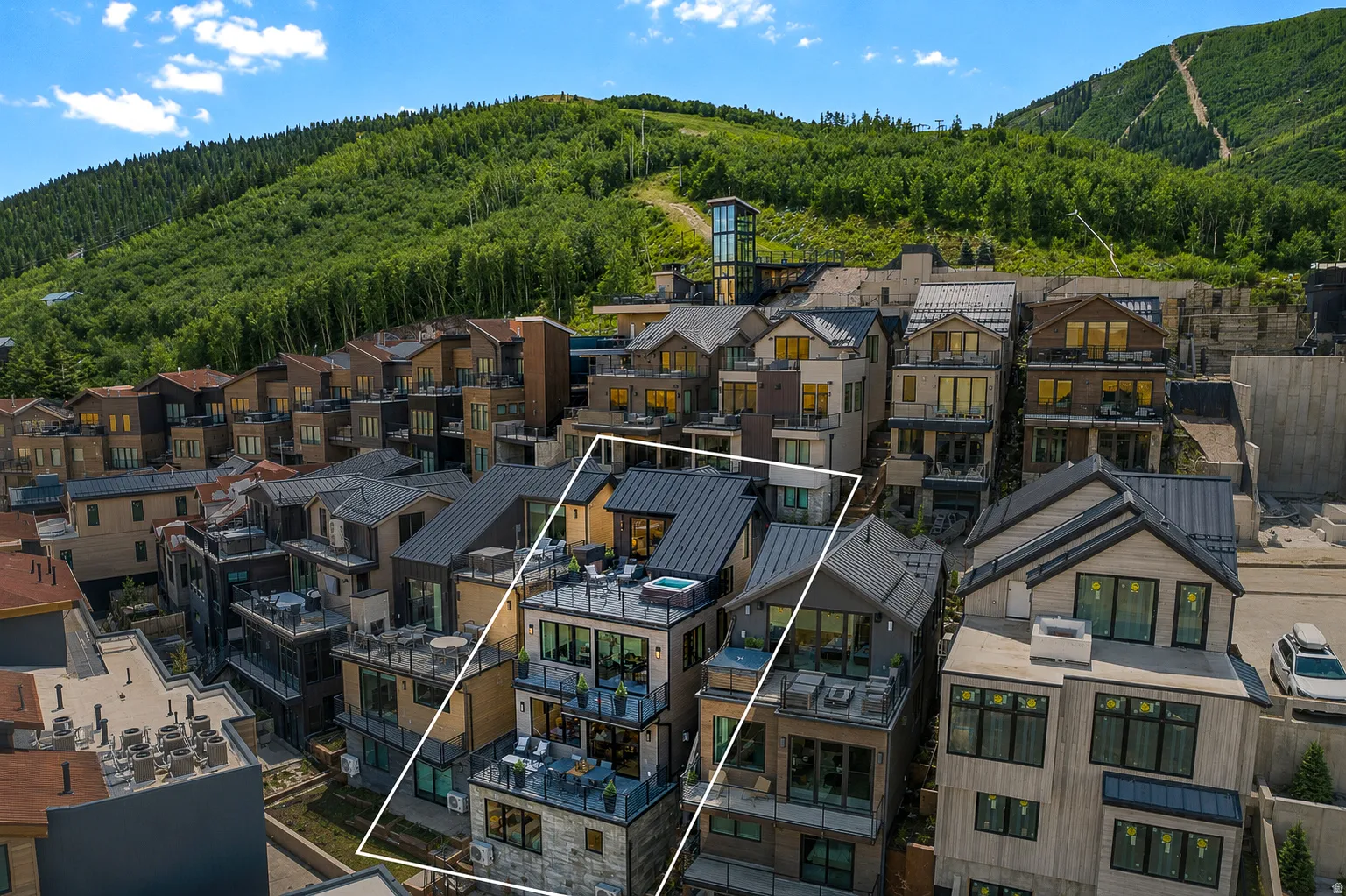 Multi-story townhouse featuring multiple balconies with glass railings, a rooftop terrace with a hot tub, and a dark metal roof