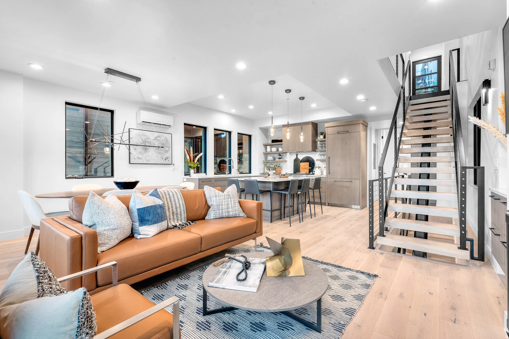 Open-concept living space featuring wood-finish flooring, recessed lighting, and a modern staircase with dark metal railings