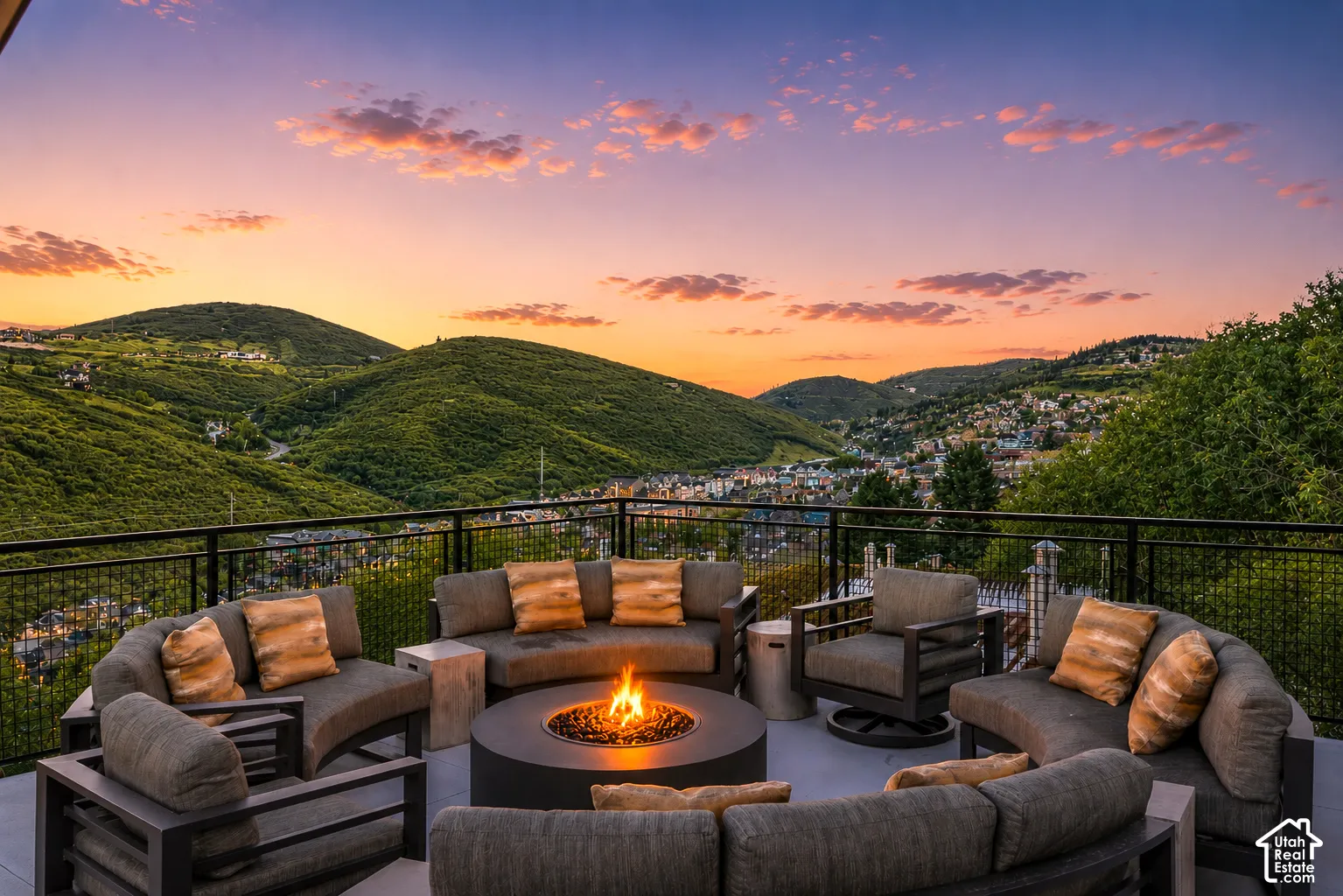 Spacious outdoor patio featuring a central fire pit, panoramic mountain scenery, and a black metal railing