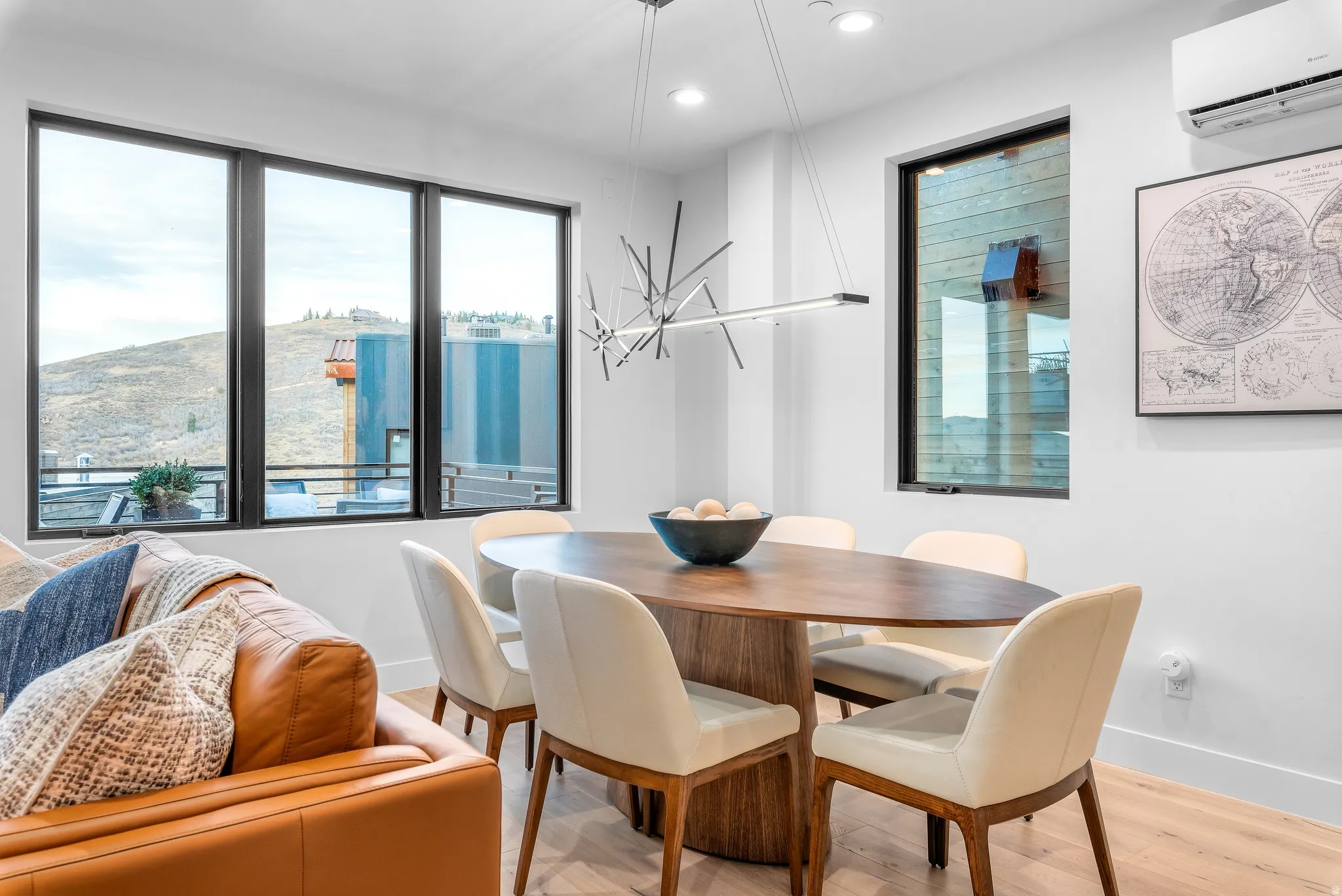 Open concept living area featuring a contemporary oval dining table with seating for six, light wood-finish flooring, a linear chandelier, recessed lighting, and large windows with black framing