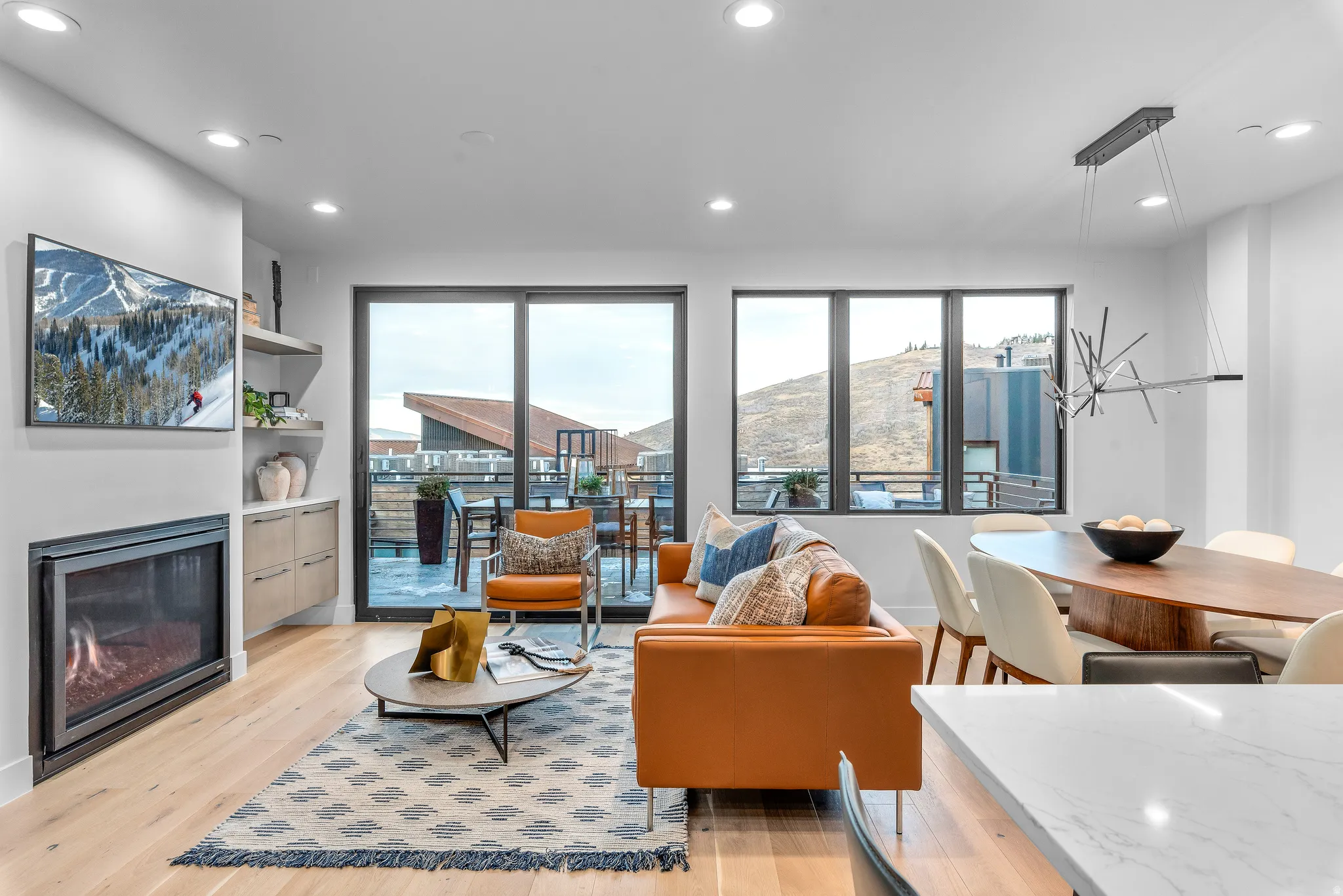 Open-concept living area featuring light wood-finish flooring, a contemporary fireplace, and built-in shelving with cabinetry