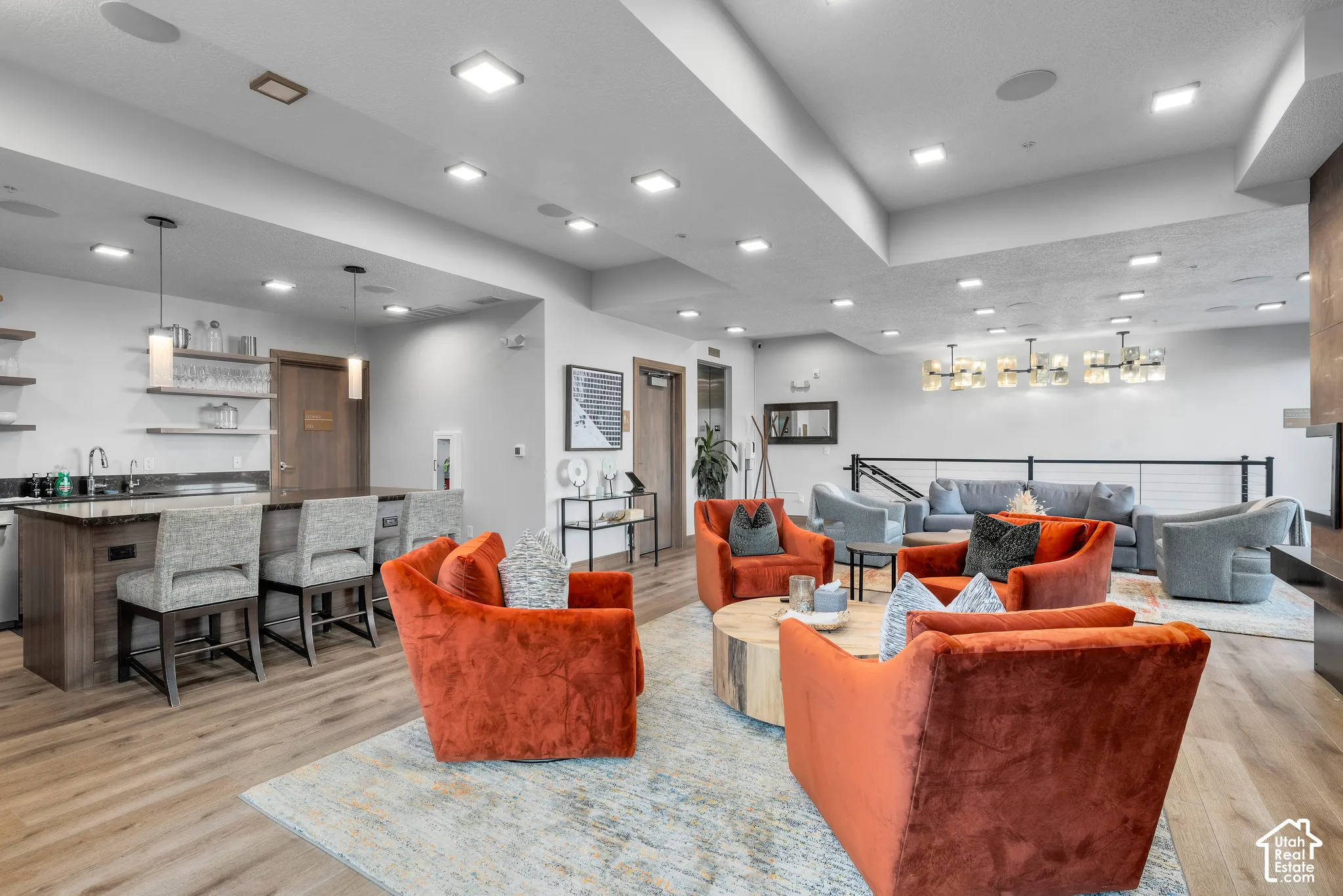 Open-concept common area featuring wood-finish flooring, a built-in wet bar with stone countertops and pendant lighting, and recessed ceiling lights