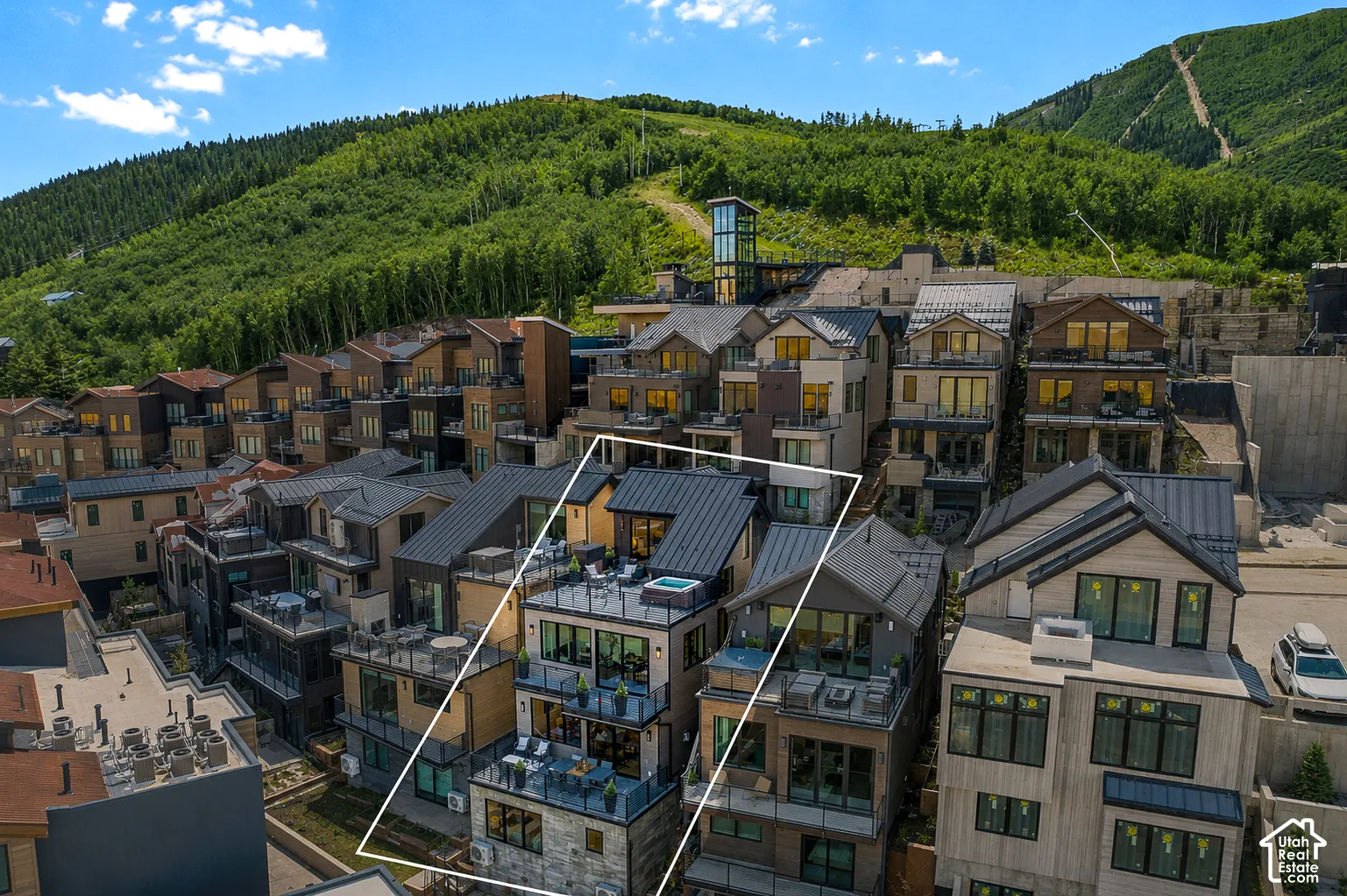 Multi-story townhouse featuring multiple balconies with glass railings, a rooftop terrace with a hot tub, and a dark metal roof