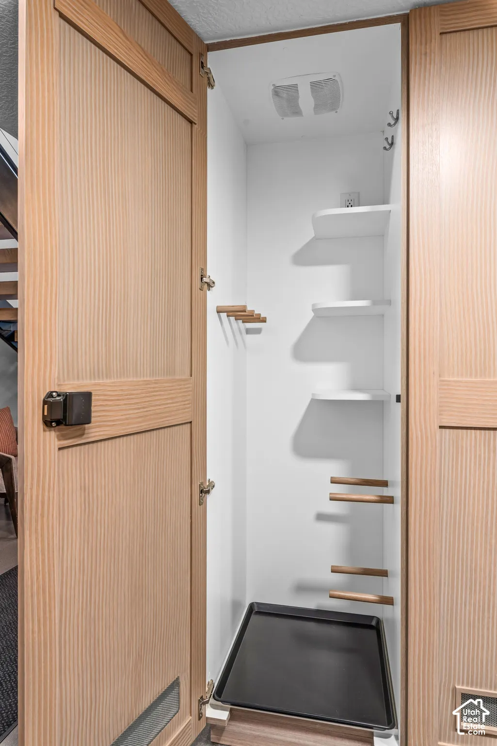 Integrated utility closet featuring light wood-finish doors, white interior shelving, and a removable bottom tray