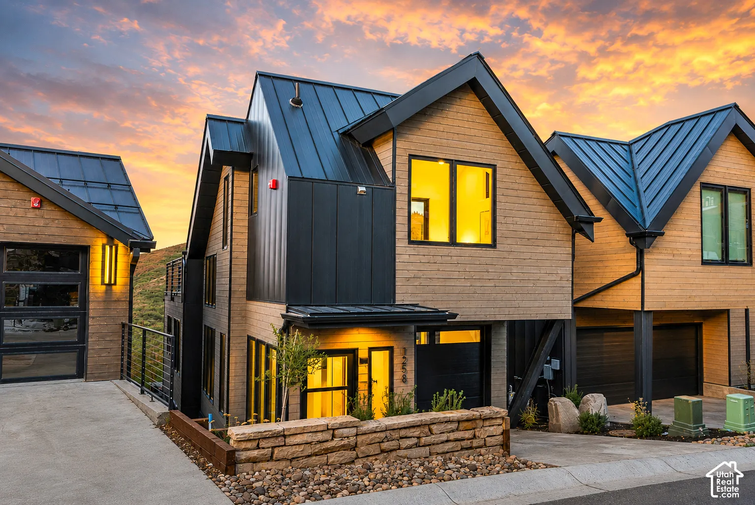 Modern architectural style featuring multiple gabled roofs with metal panels, wood-look siding, and dark vertical paneling