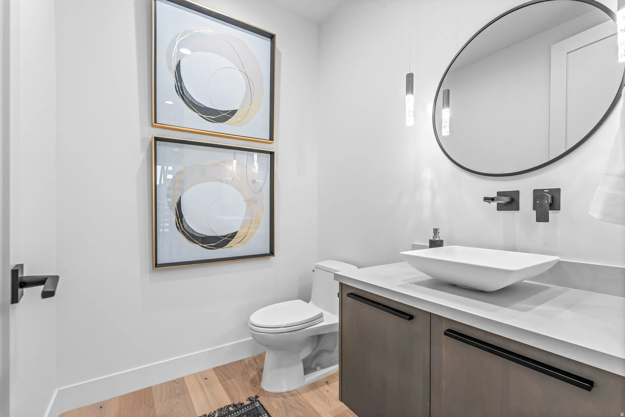 Contemporary powder room featuring a floating vanity with a vessel sink, wall-mounted matte black faucet, and a round black-framed mirror