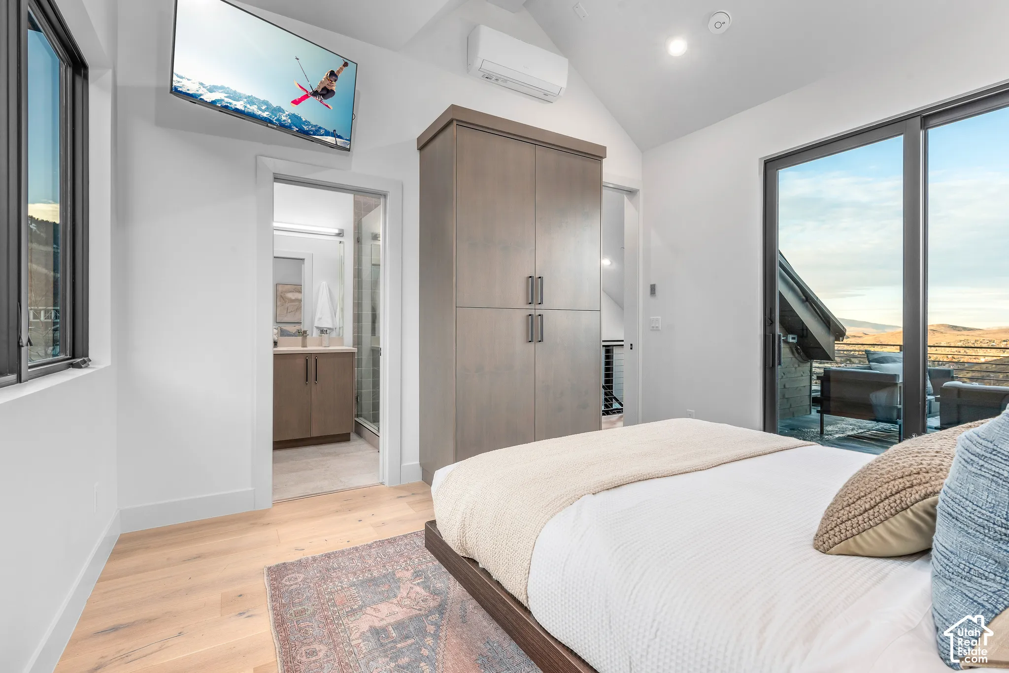 Vaulted ceiling room featuring light wood-finish flooring, a built-in wardrobe, and sliding glass doors opening to an exterior area