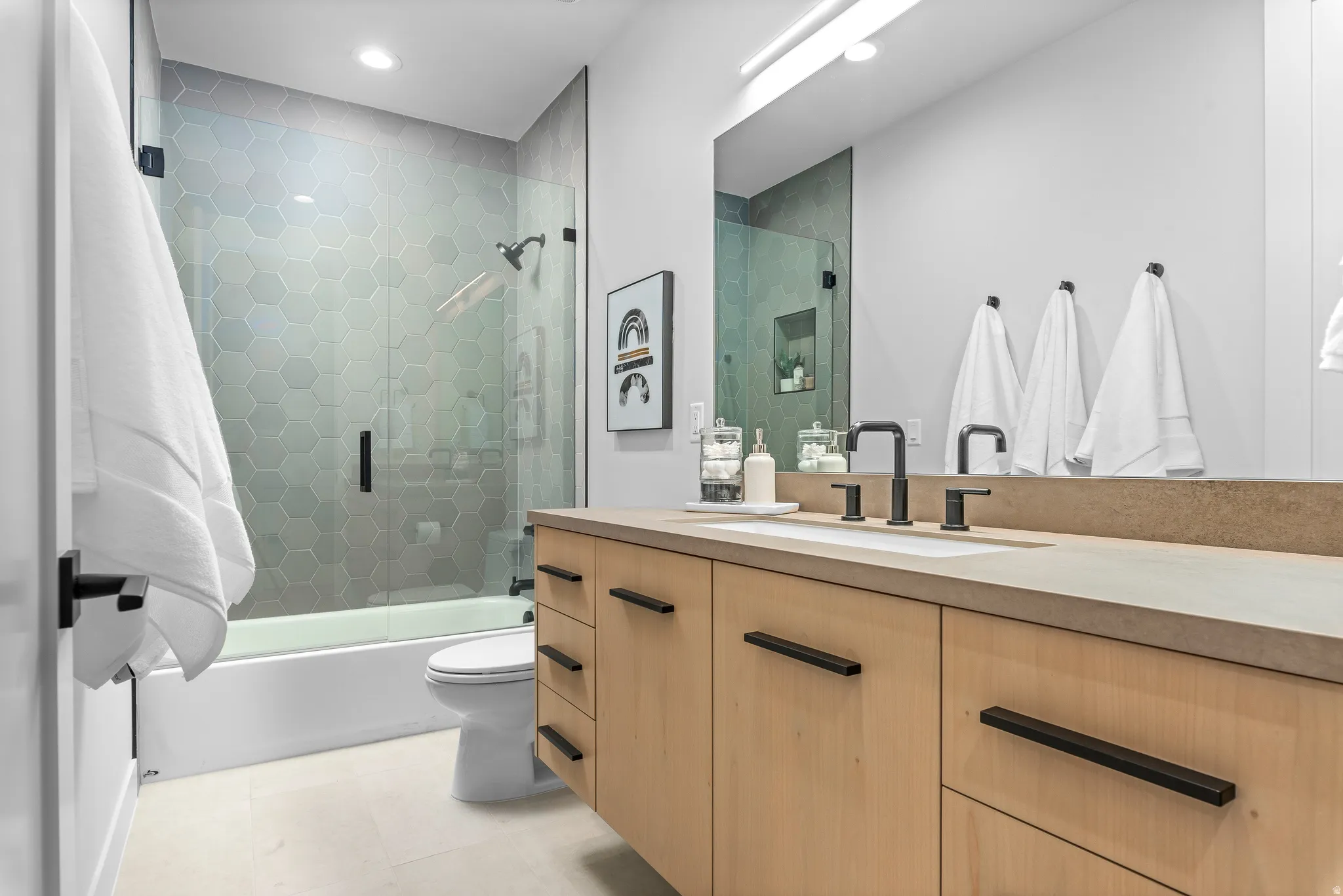Contemporary bathroom featuring a light wood-finish vanity with a stone-finish countertop and integrated sink