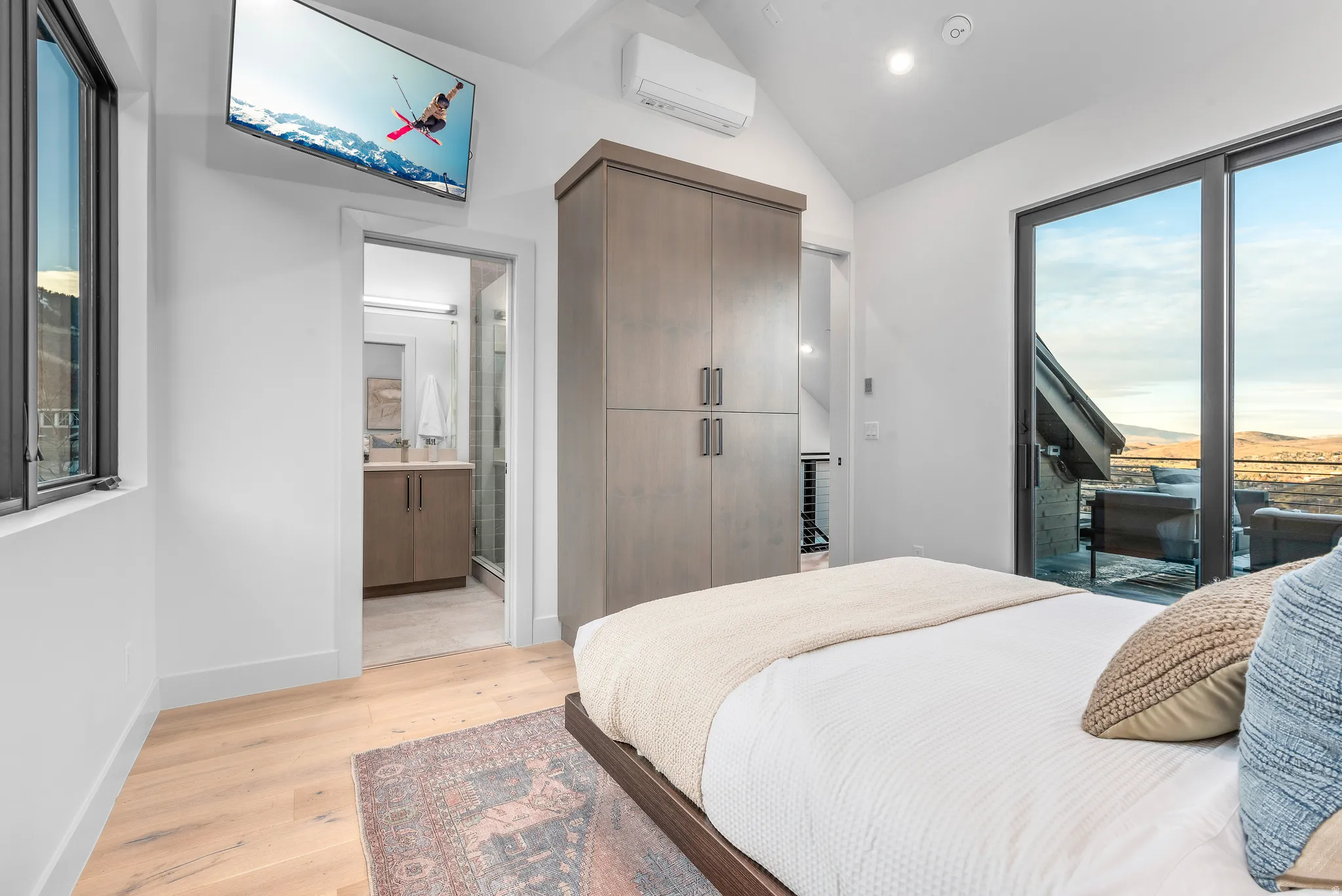 Vaulted ceiling room featuring light wood-finish flooring, a built-in wardrobe, and sliding glass doors opening to an exterior area