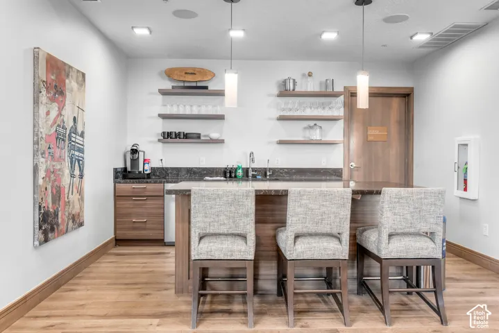 Wet bar featuring wood-finish flooring, dark stone countertops, wood cabinetry, and open shelving