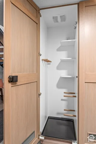 Integrated utility closet featuring light wood-finish doors, white interior shelving, and a removable bottom tray