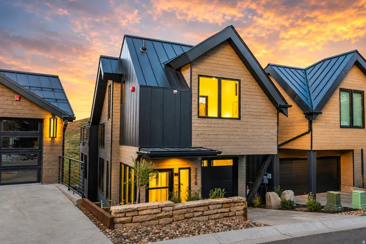 Modern architectural style featuring multiple gabled roofs with metal panels, wood-look siding, and dark vertical paneling