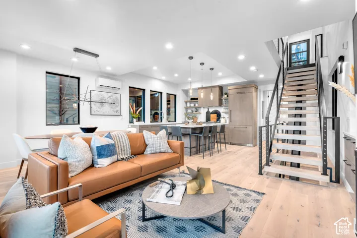 Open-concept living space featuring wood-finish flooring, recessed lighting, and a modern staircase with dark metal railings