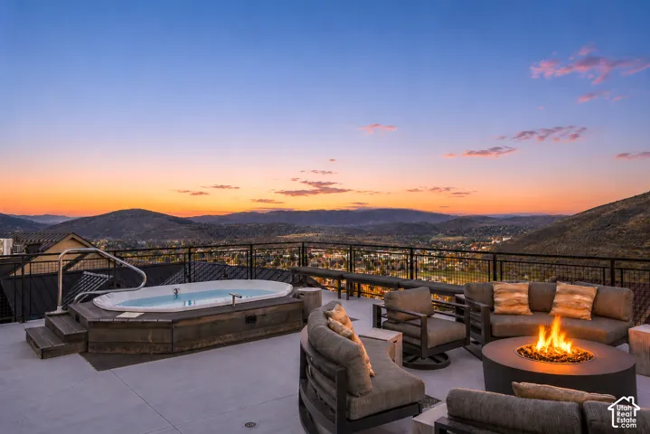 Expansive outdoor patio featuring a built-in hot tub with steps, a gas fire pit, and metal railings