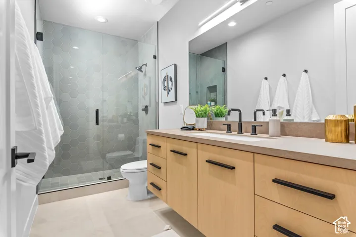 Contemporary bathroom featuring a glass-enclosed shower with hexagon tile surround, a light wood-finish vanity with ample storage, a solid surface countertop, and black fixtures