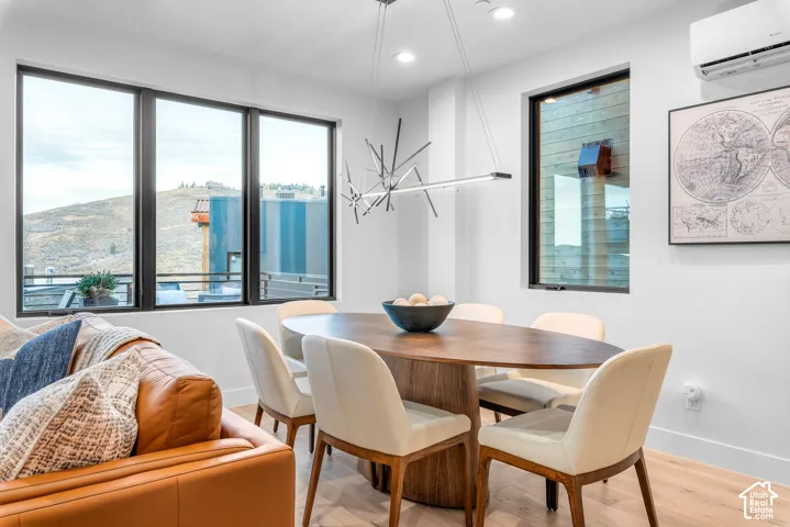 Open concept living area featuring a contemporary oval dining table with seating for six, light wood-finish flooring, a linear chandelier, recessed lighting, and large windows with black framing